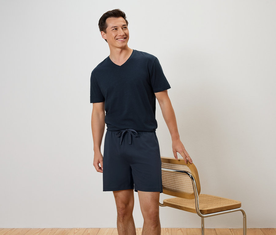 Ein Mann steht neben einem Stuhl und trägt ein marineblaues T-Shirt und Shorts.