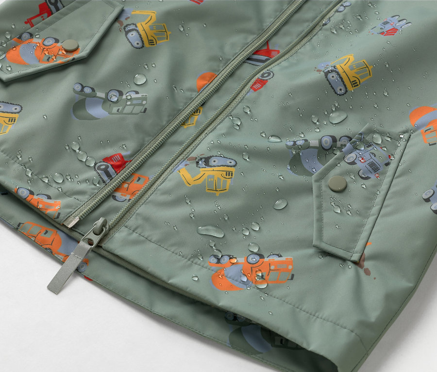 Nahaufnahme einer olivgrünen Jacke mit Reißverschluss und Bauarbeiter-Motiv, bedeckt mit Wassertropfen.