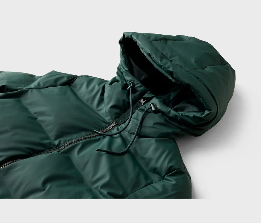 Nahaufnahme einer dunkelgrünen Steppjacke mit Kapuze, die einen schwarzen Reißverschluss und schwarze Kordelzüge mit Stoppern zeigt.