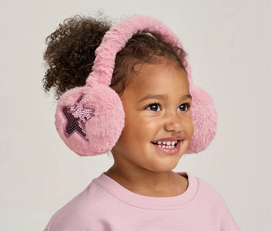 Lächelndes Kind mit lockigem Haar trägt rosa flauschige Ohrenschützer mit Paillettensternen.