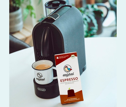 Eine Tasse Kaffee steht auf einer DeLonghi Maschine, daneben eine Packung earlybird Bio Espresso Kapseln.