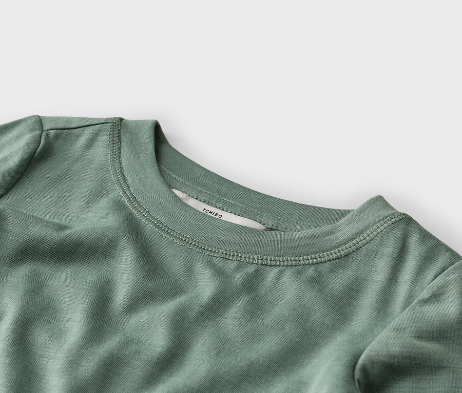 Nahaufnahme eines salbeigrünen T-Shirts, das den gerippten Rundhalsausschnitt mit sichtbaren Nähten und ein weißes "TCHIBO"-Etikett im Nacken zeigt.