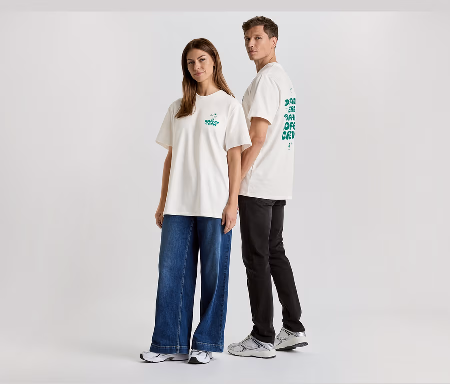 Eine Frau in Jeans und ein Mann in schwarzer Hose, beide tragen weiße T-Shirts mit Aufdruck.