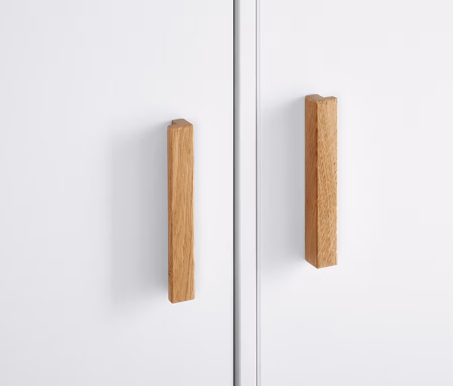 Detailansicht eines weißen Kleiderschranks mit Holzgriffen.