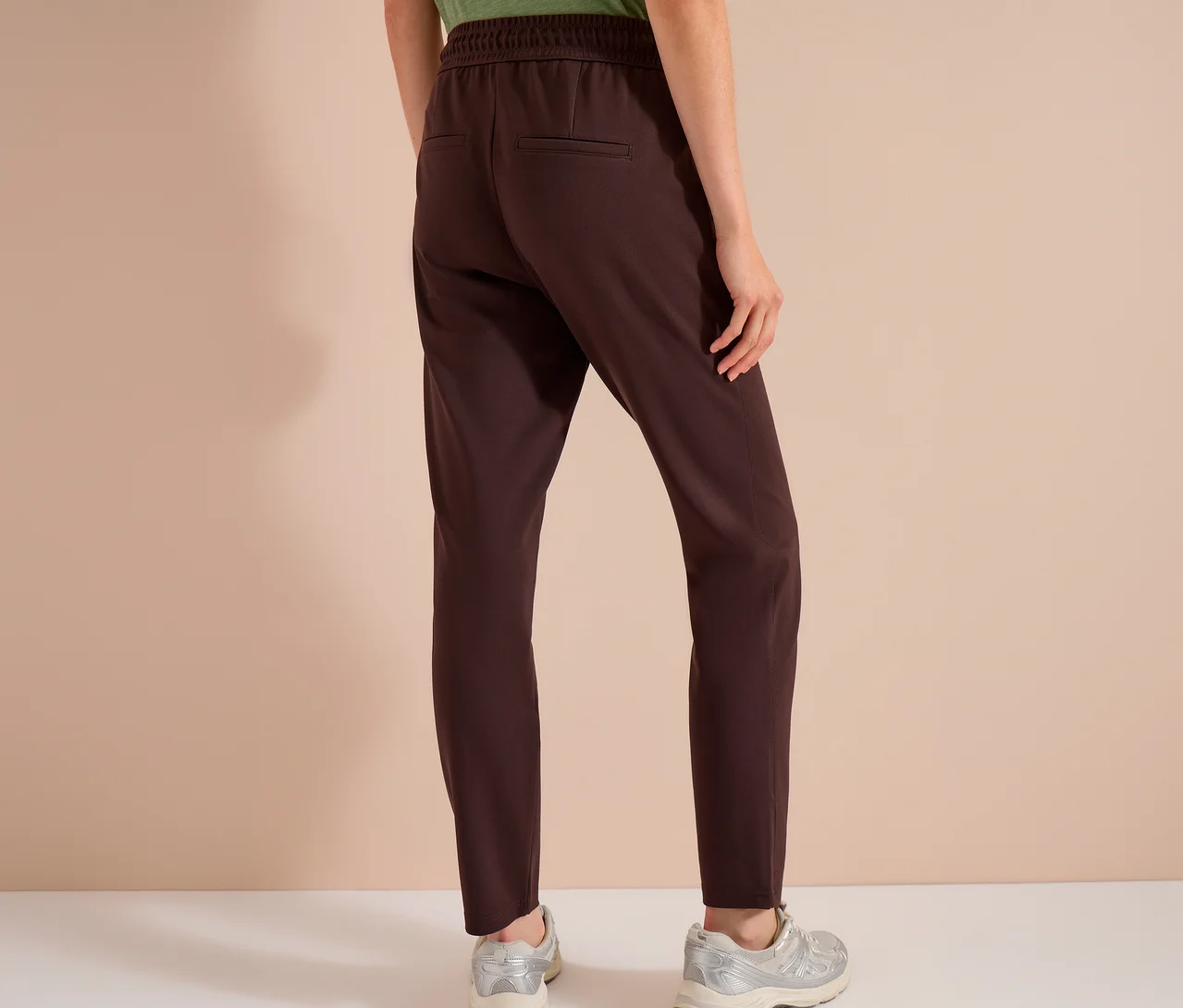 Person von hinten in brauner CECIL Jerseyhose mit Gummibund und zwei Gesäßtaschen, dazu silberne Sneaker.