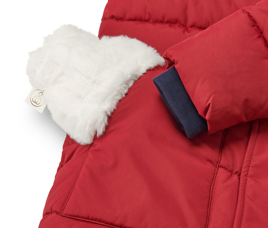 Detail einer roten Jacke mit einer Mini-Wärmflasche mit weißem Plüschbezug in der Tasche.