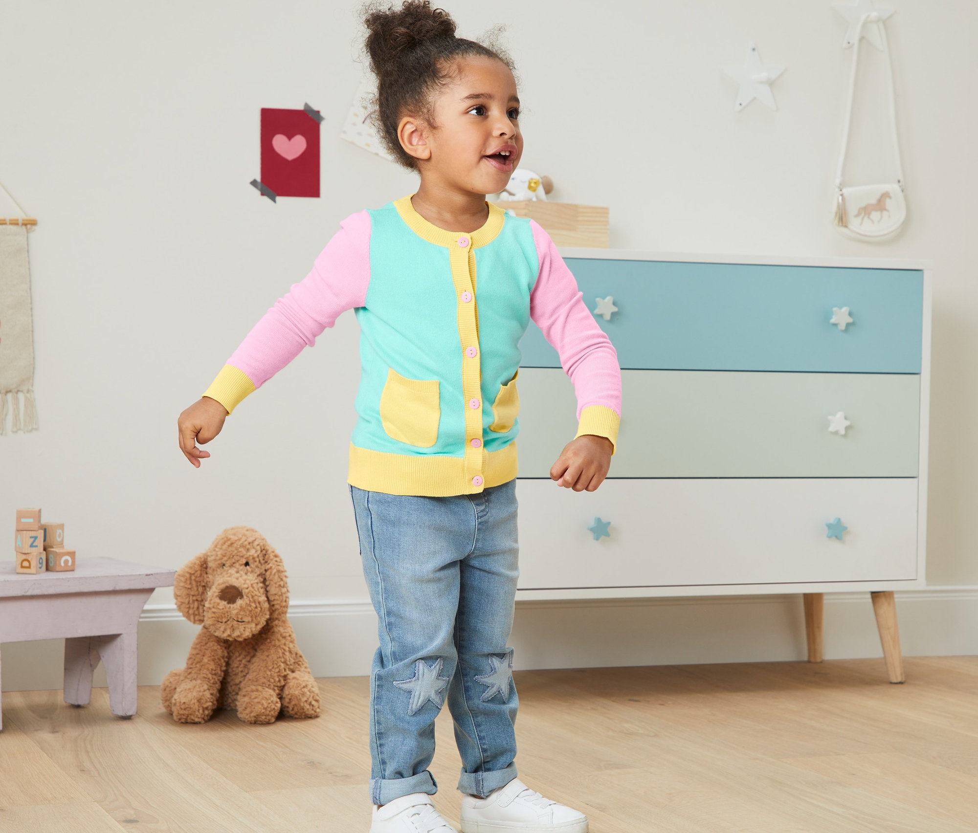 Mädchen trägt eine Strickjacke mit Bio-Baumwolle im Kinderzimmer.