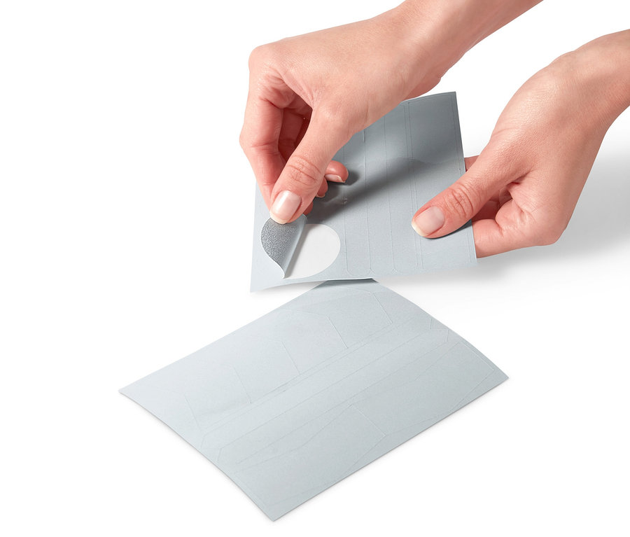 Hände lösen einen reflektierenden Aufkleber von einem Bogen mit 16 reflektierenden Aufklebern.