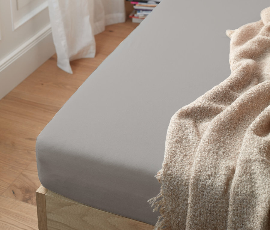 Graues Jersey-Spannbettlaken Normalgröße auf einem Bett mit einer beigen Decke.
