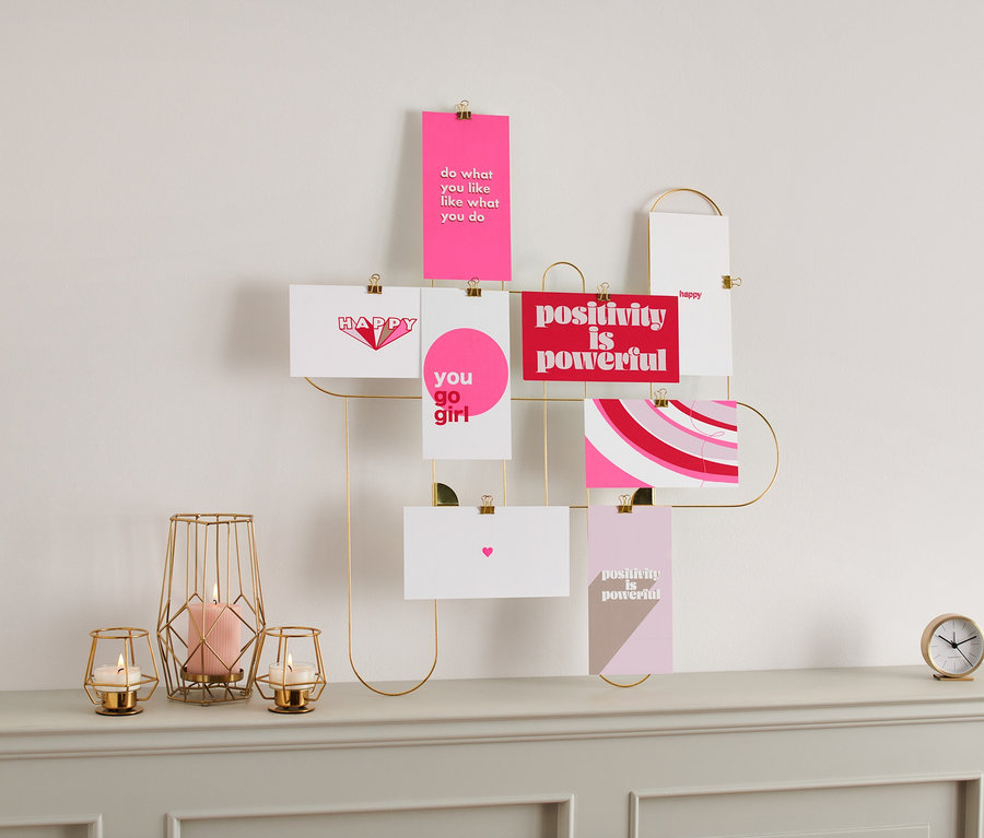 Ein Postkarten-/Minibilder-Set hängt an einem goldenen Rahmen an der Wand. Kerzen und eine Uhr stehen auf einer Kommode.