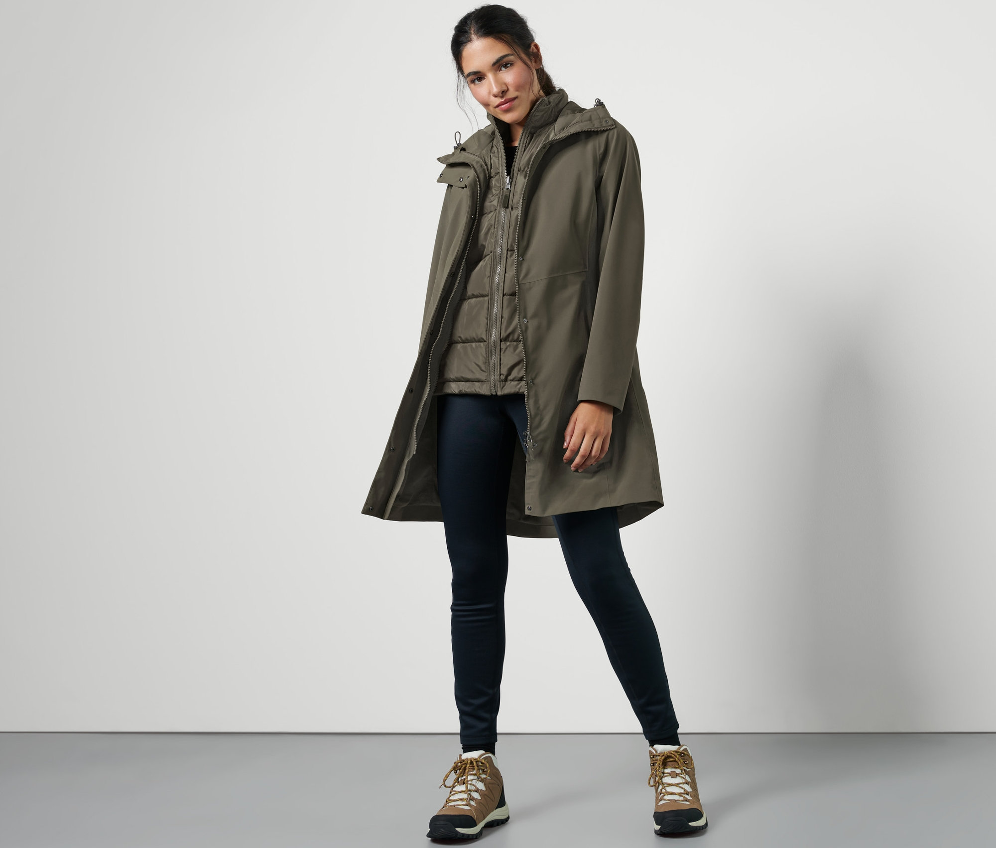 Eine Frau posiert in einem 3-in-1-Regenmantel mit Weste, dunklen Jeans und Wanderstiefeln.