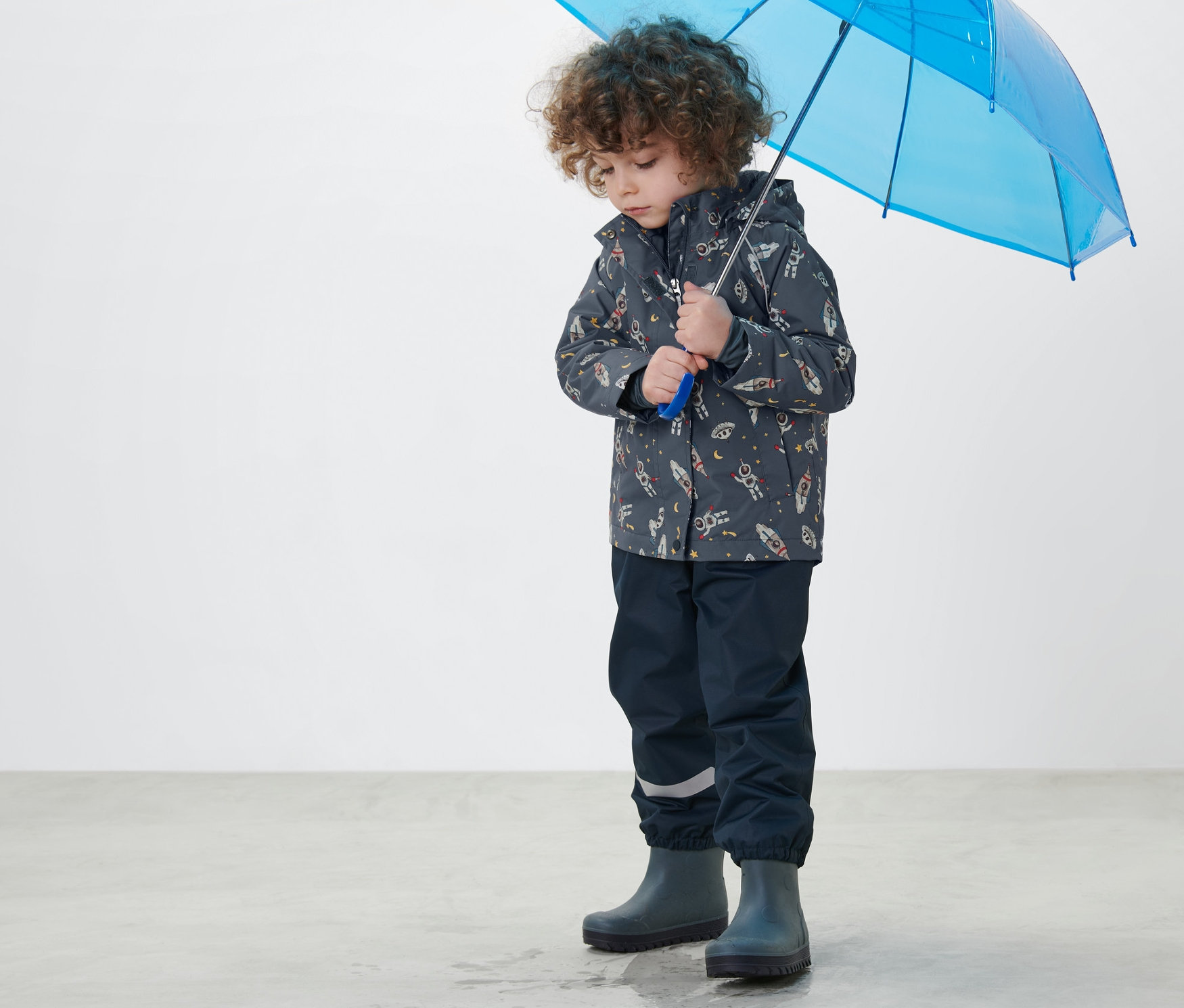 Junge hält blauen Regenschirm und trägt dunkelblaue Kinder-Thermo-Regenjacke.