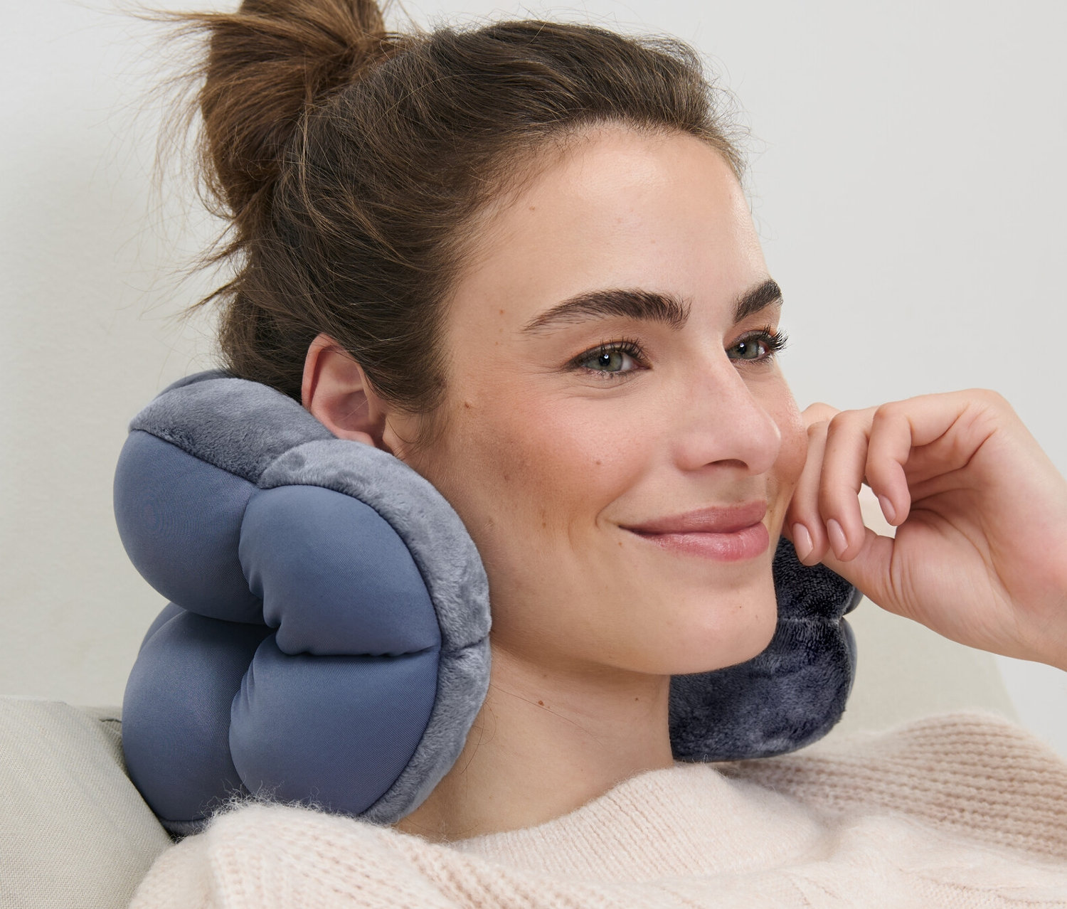 Frau sitzt mit Relaxkissen im Nacken auf einem Sofa.