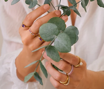 Frau hält Eukalyptuszweige und trägt 925 Silber Ringe, Multicolor Ring, 375 und 585 Gold Ring Amethyst, Doppel-Welle mit Kristallen Ring und pavé Ring.