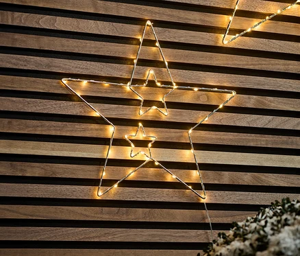Zwei kleine LED-Metallsterne hängen an einer Holzwand.