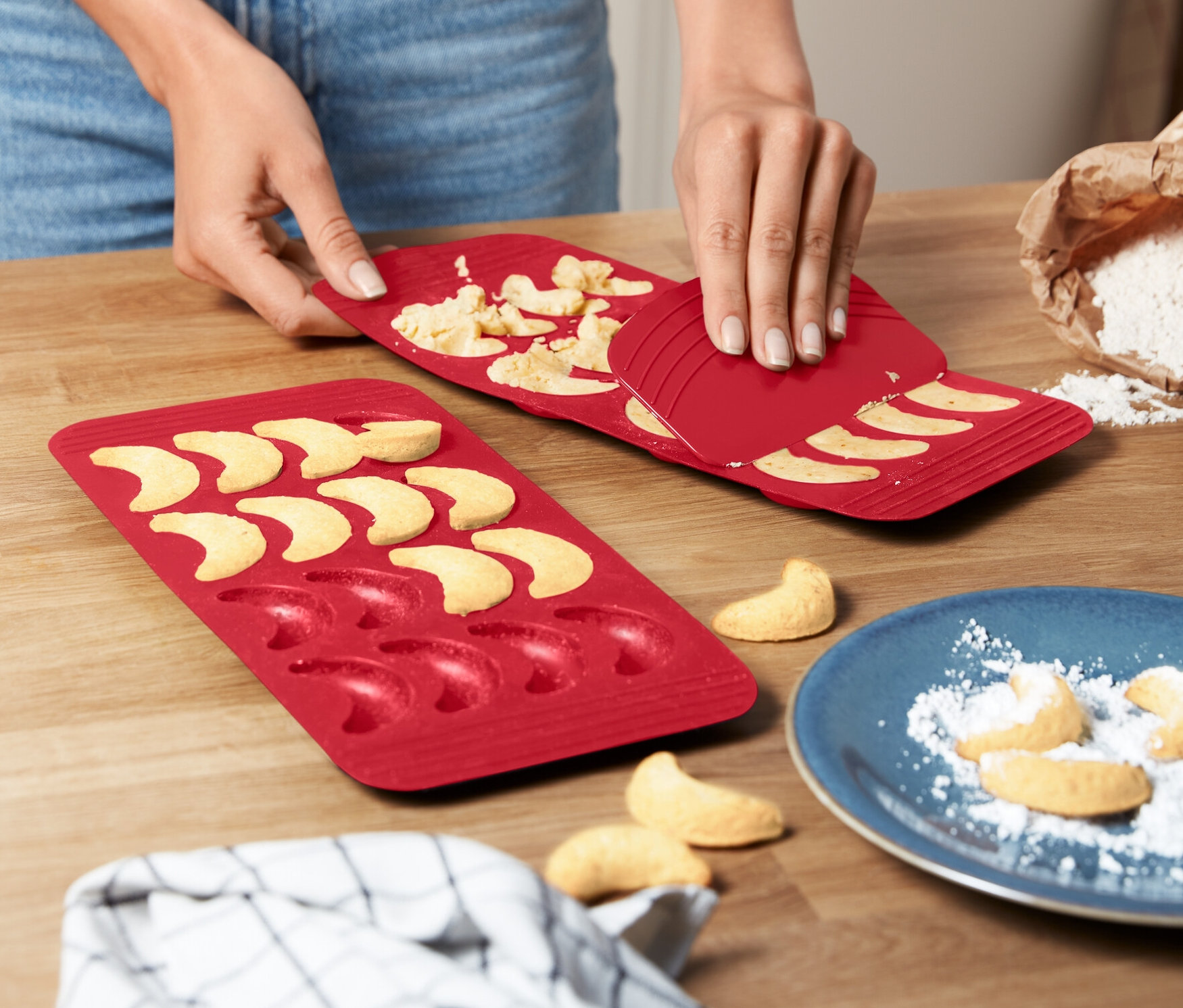 Eine Frau löst Vanillekipferl aus einer roten 2 Vanillekipferl-Backmatte.