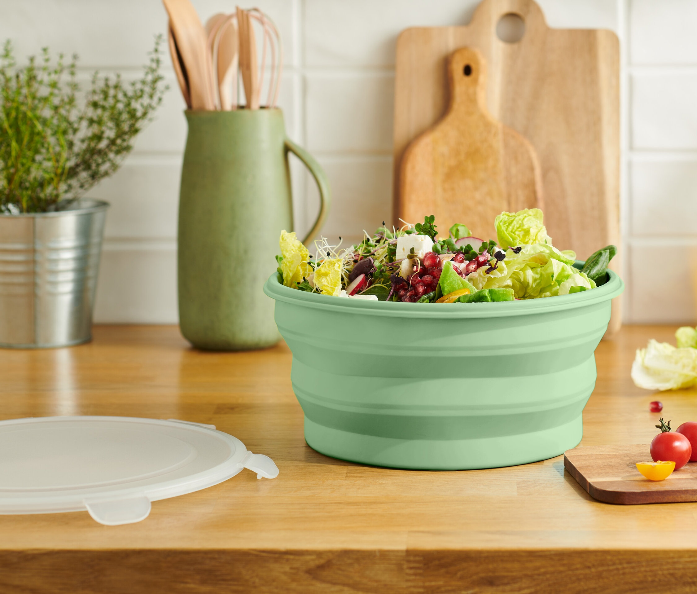 Eine grüne, faltbare Salatschüssel gefüllt mit Salat steht auf einer hölzernen Küchentheke.