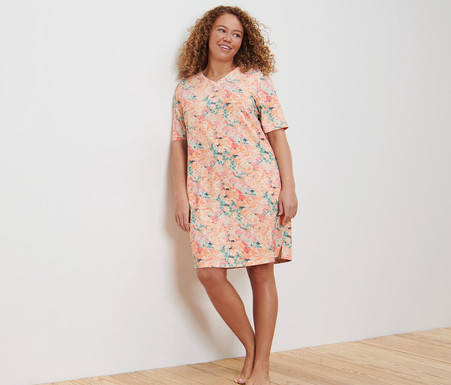 Frau lehnt in einem Nachthemd an der Wand.