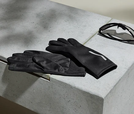 Schwarze Handschuhe und Sonnenbrille liegen auf einer grauen Betonoberfläche.