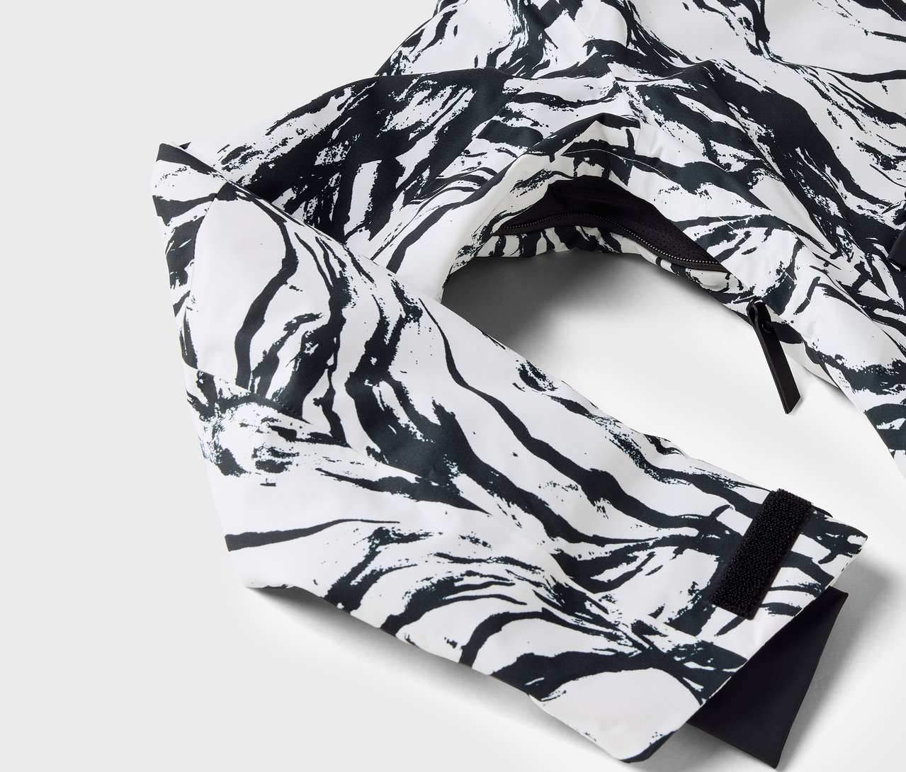 Detailaufnahme einer weißen Jacke mit schwarzem Muster, Ärmel und Reißverschluss sichtbar.