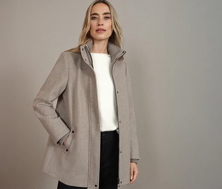Frau trägt einen Street One Kurzmantel in Beige, kombiniert mit einem weißen Oberteil und einer schwarzen Hose.