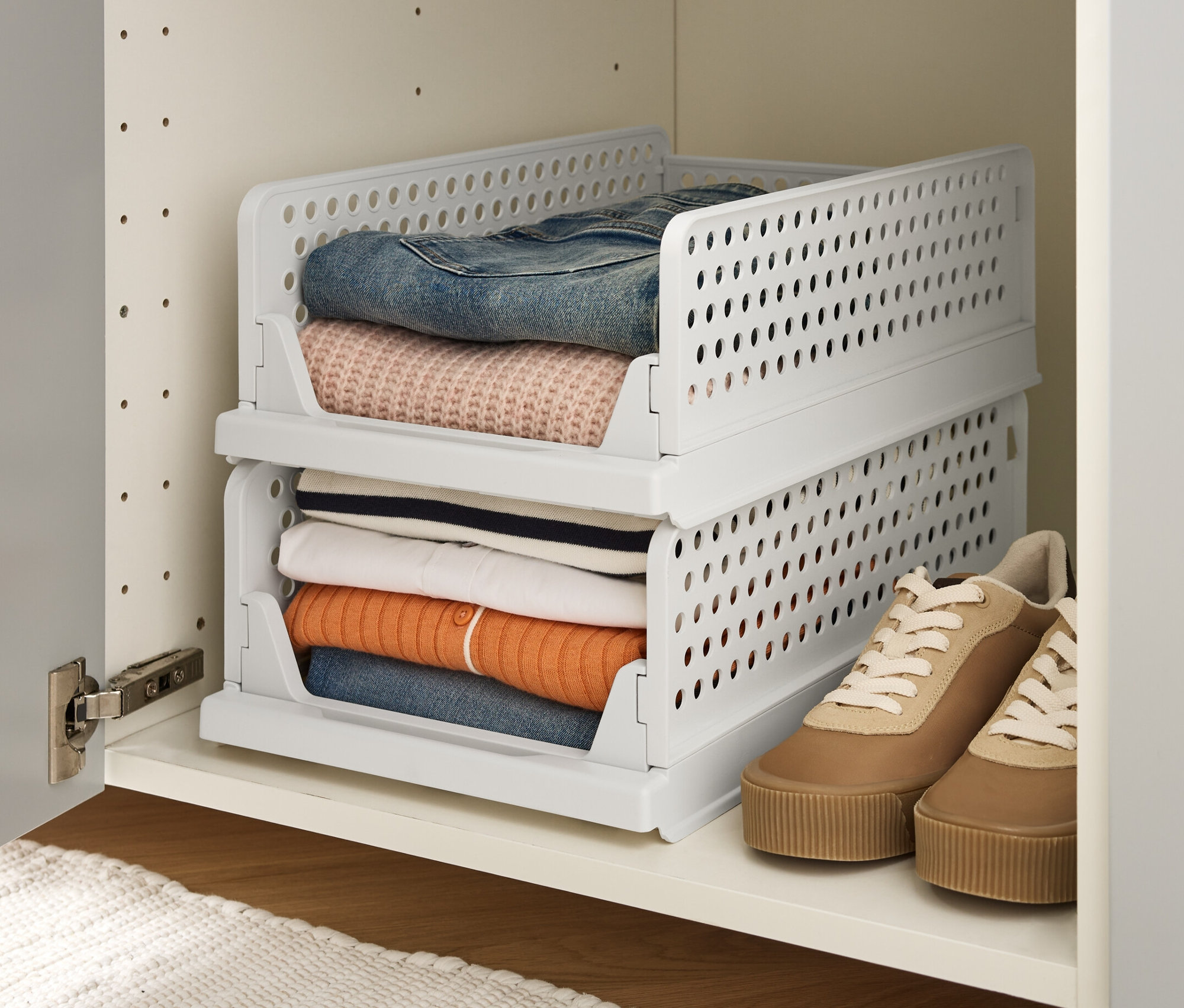 Zwei stapelbare Klappboxen in Weiß stehen in einem weißen Schrank und sind mit Kleidung gefüllt.