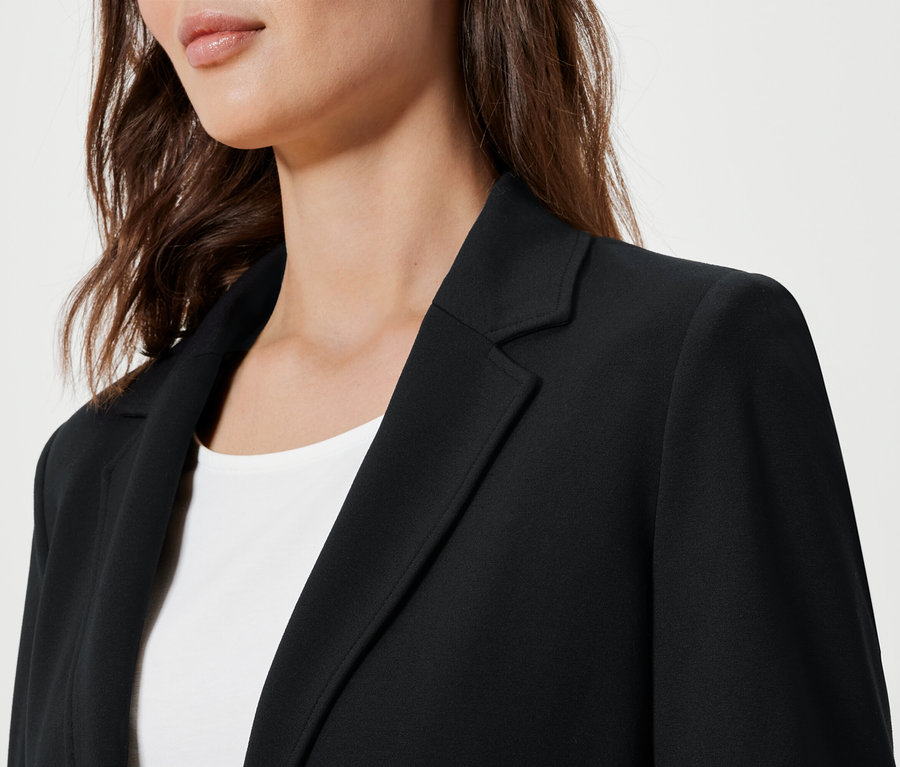 Detail einer Frau, die einen schwarzen Jerseyblazer trägt.