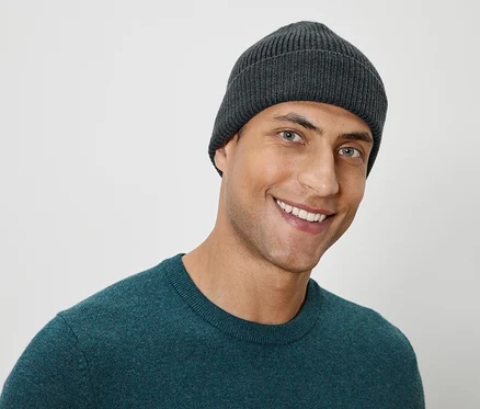 Porträt eines lächelnden Mannes mit einer grauen Strickmütze und einem grünen Pullover.