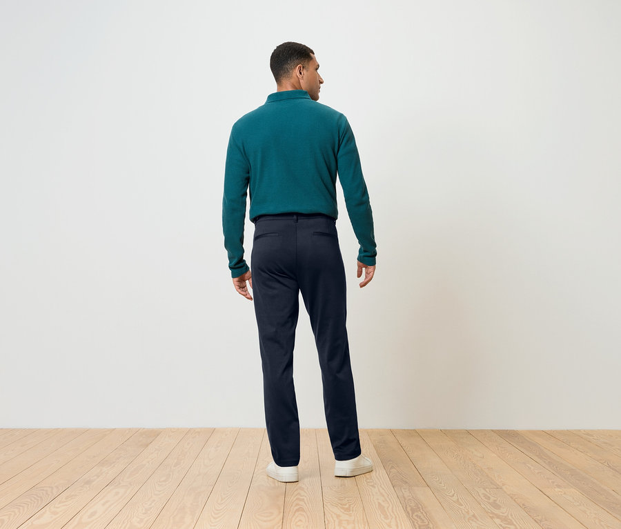 Mann von hinten trägt blaue Hosen und ein grünes Langarmshirt.