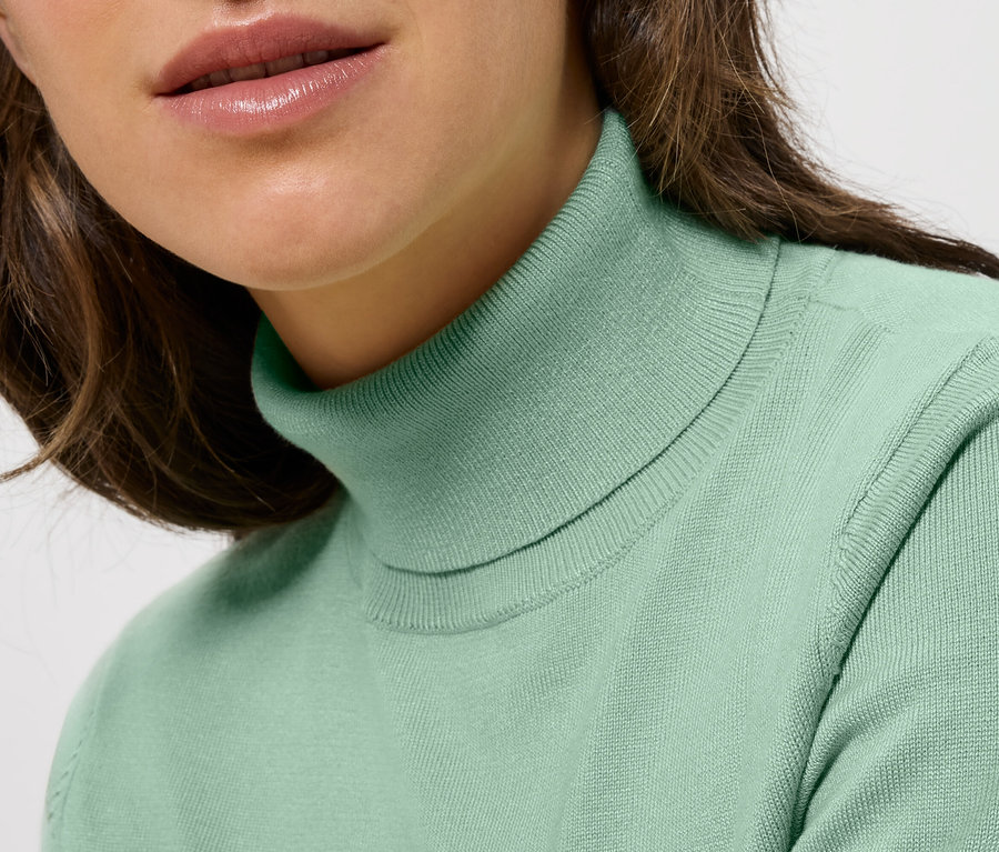 Detailaufnahme einer Dame mit braunem Haar, die einen mintgrünen Rollkragenpullover trägt.