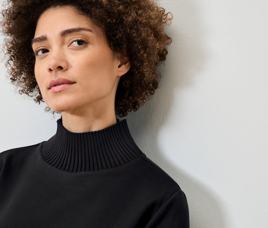 Porträt einer Frau mit lockigem Haar in einem schwarzen Rollkragenpullover.