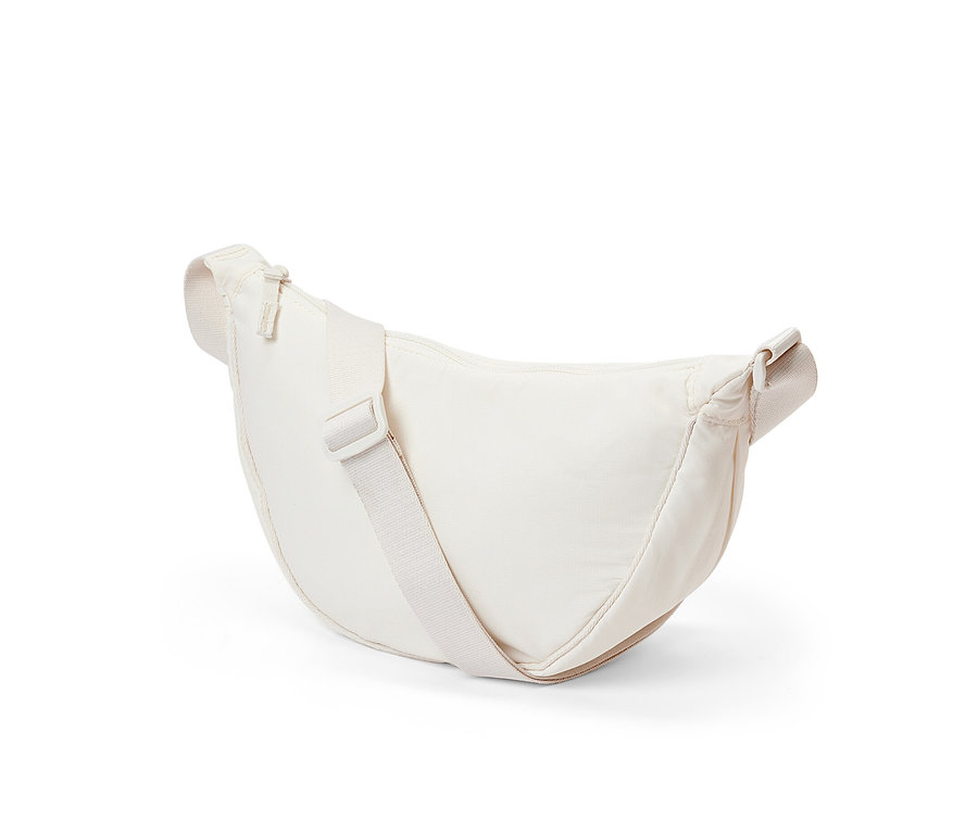 Eine cremefarbene Umhängetasche liegt auf einem weißen Hintergrund.
