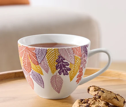 Eine Tasse Tee mit herbstlichem Blättermotiv und zwei Schokoladenkekse auf einem Holztablett.