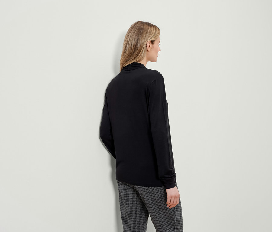 Eine von hinten gezeigte Frau trägt ein schwarzes Langarmshirt und eine Hose mit Hahnentrittmuster.