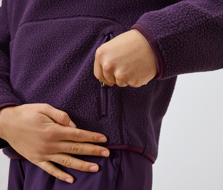 Person schliesst den Reissverschluss einer violetten Fleecejacke.