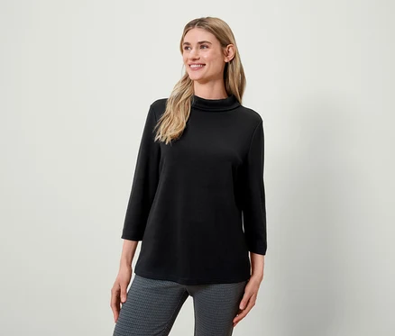 Blonde Frau mit schwarzem Rollkragenpullover und grau gemusterter Hose lächelt und schaut nach links.