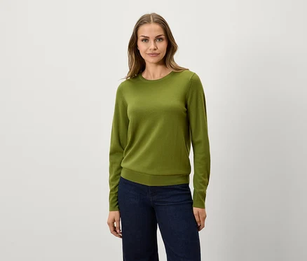 Eine Frau trägt einen olivgrünen Pullover und dunkelblaue Jeans.
