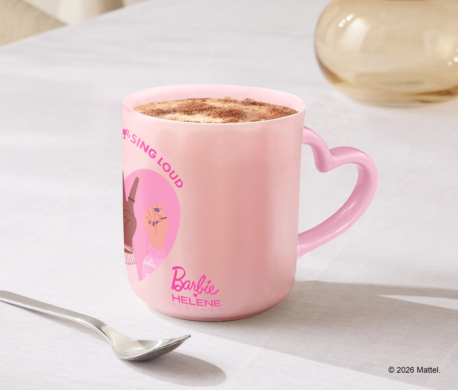 Eine rosafarbene Tasse mit Herzgriff steht auf einem Tisch neben einem Löffel und Keksen.