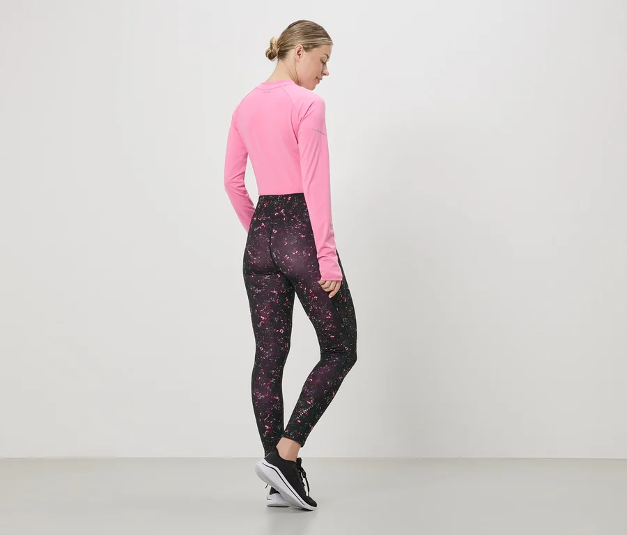 Eine Frau steht mit dem Rücken zum Betrachter, trägt ein pinkes Langarmshirt, Leggings mit Muster und schwarze Turnschuhe.