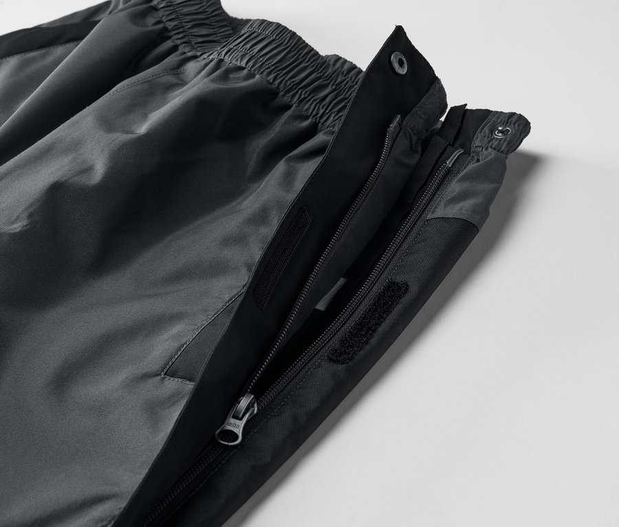 Nahaufnahme einer grauen Hose mit teilweise geöffnetem Reißverschluss und Druckknopfverschluss.