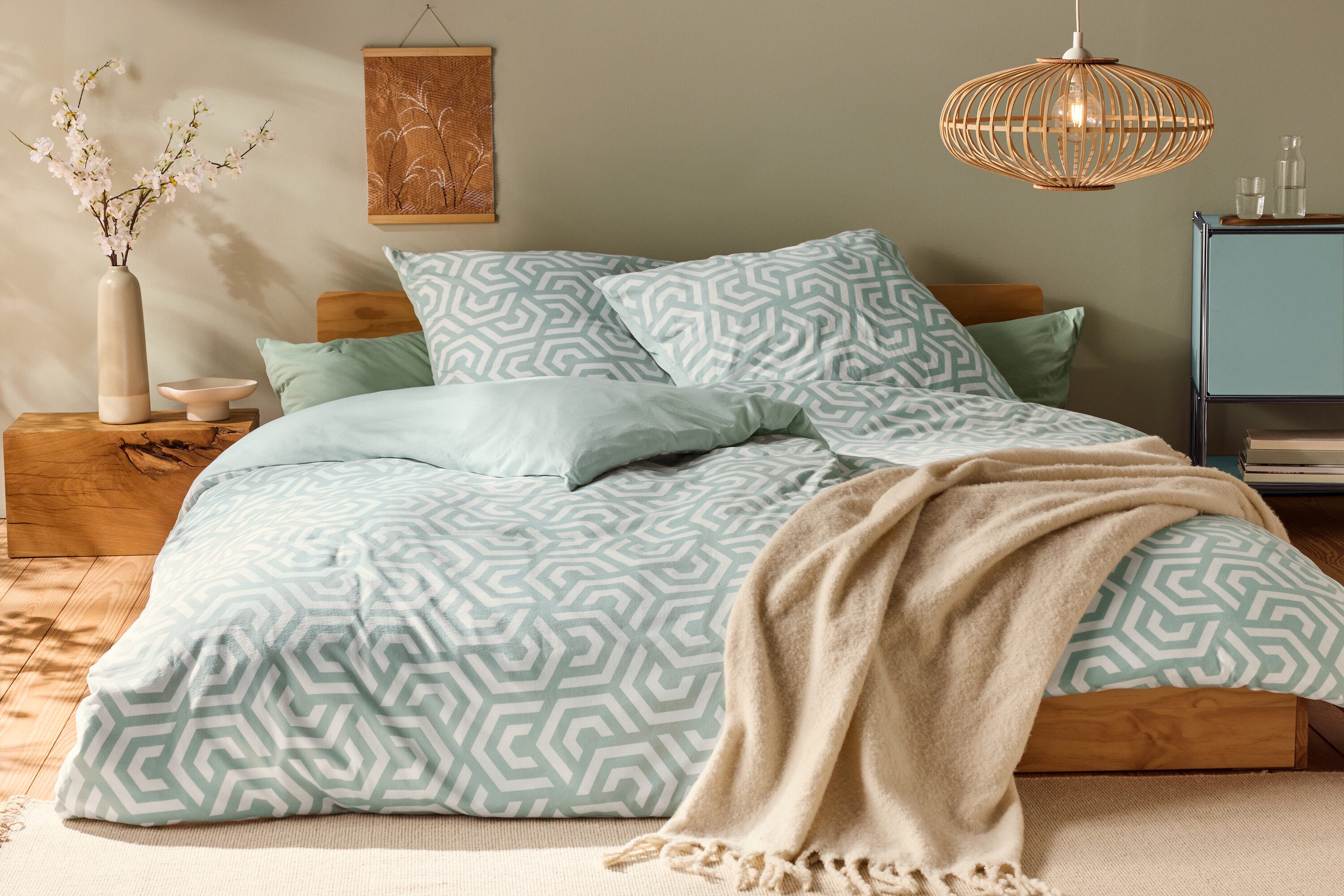 Bett mit Jersey-Bettwäsche, Normalgröße, mit geometrischem Muster und hellgrünen Kissen.