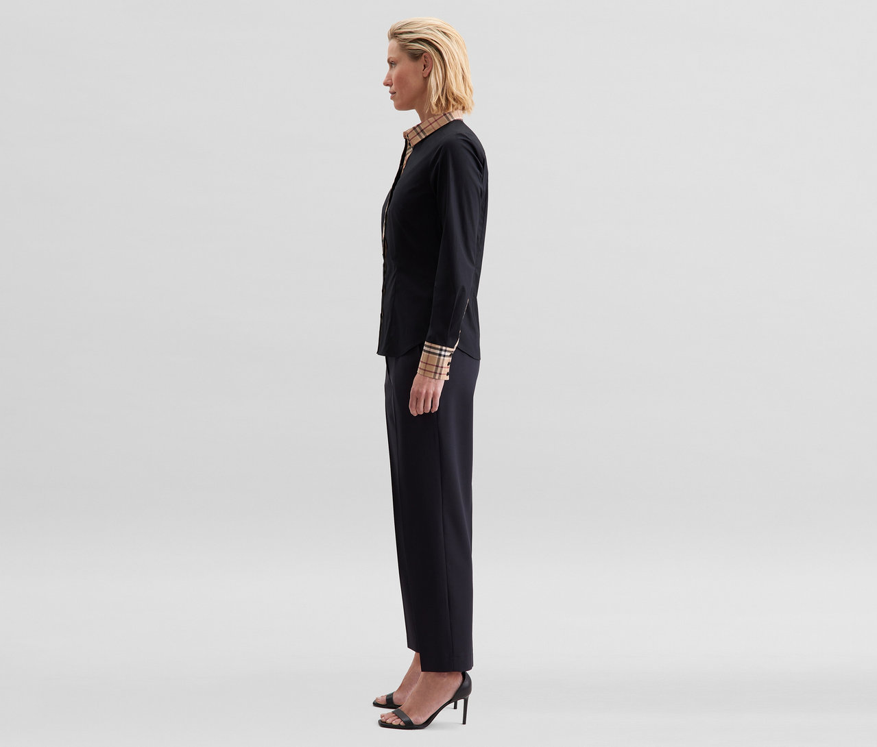 Frau im Profil trägt eine schwarze Seidensticker Popeline-Bluse mit Karodetail an Kragen und Manschetten, schwarze Hose und schwarze Sandalen.