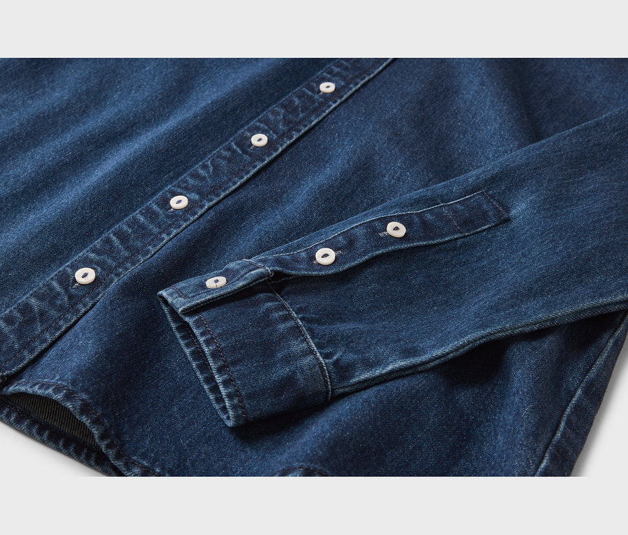 Nahaufnahme eines dunkelblauen Jeanshemdes, das die Knopfleiste mit weißen Knöpfen und einen Ärmelbund mit weißen Knöpfen zeigt.