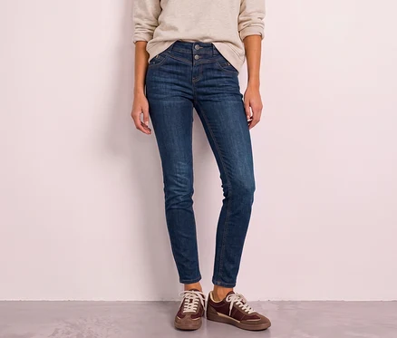 Person steht, trägt dunkelblaue Street One Jeans mit hohem Bund und braune Sneaker.
