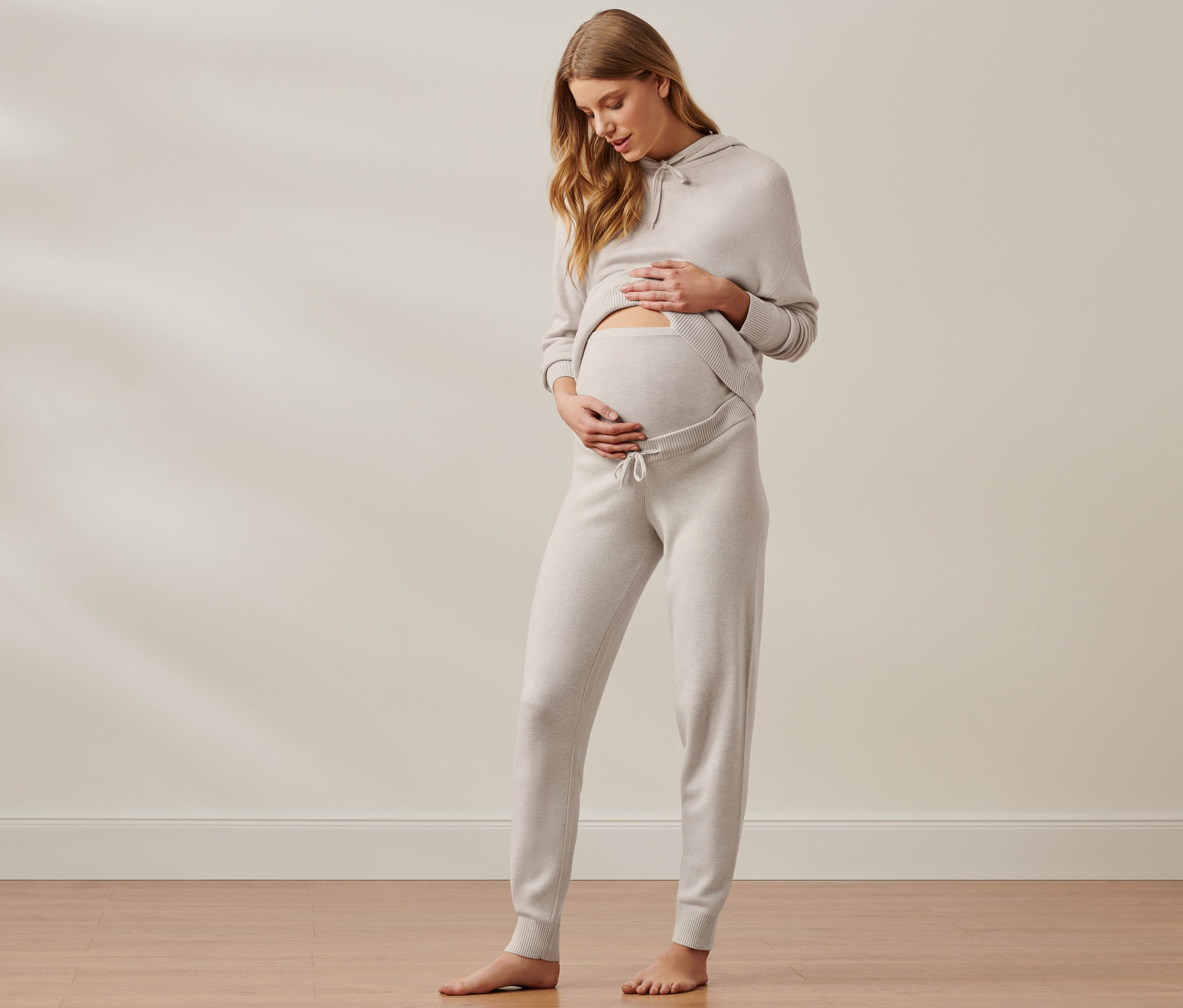 Schwangere Frau streichelt ihren Bauch in Umstands-Loungekombination.