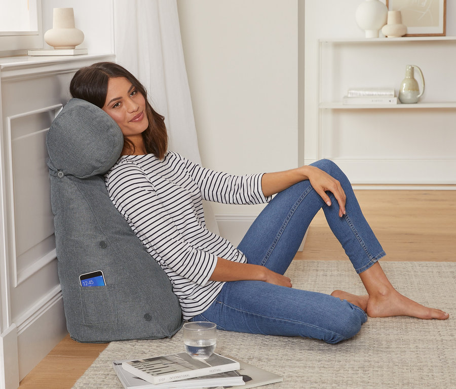 Frau sitzt angelehnt an einem grauen Rückenkissen mit Nackenrolle.