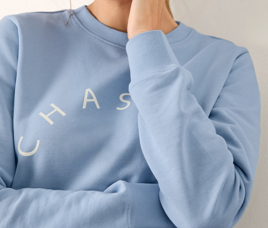 Frau berührt ihren Hals und trägt ein hellblaues Sweatshirt mit Print.