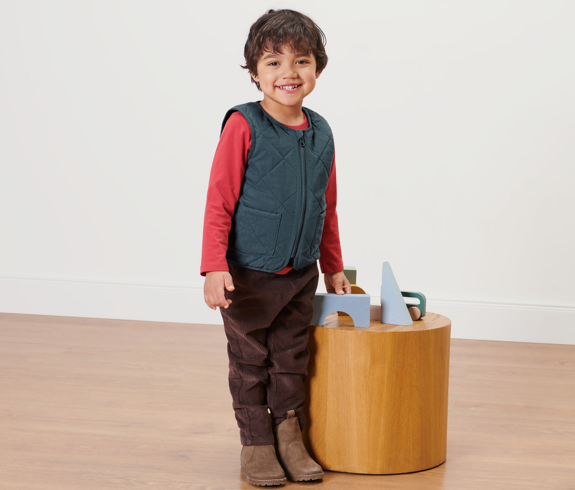 Ein Junge steht neben einem Holztisch und trägt eine Kinder-Wendesteppweste.