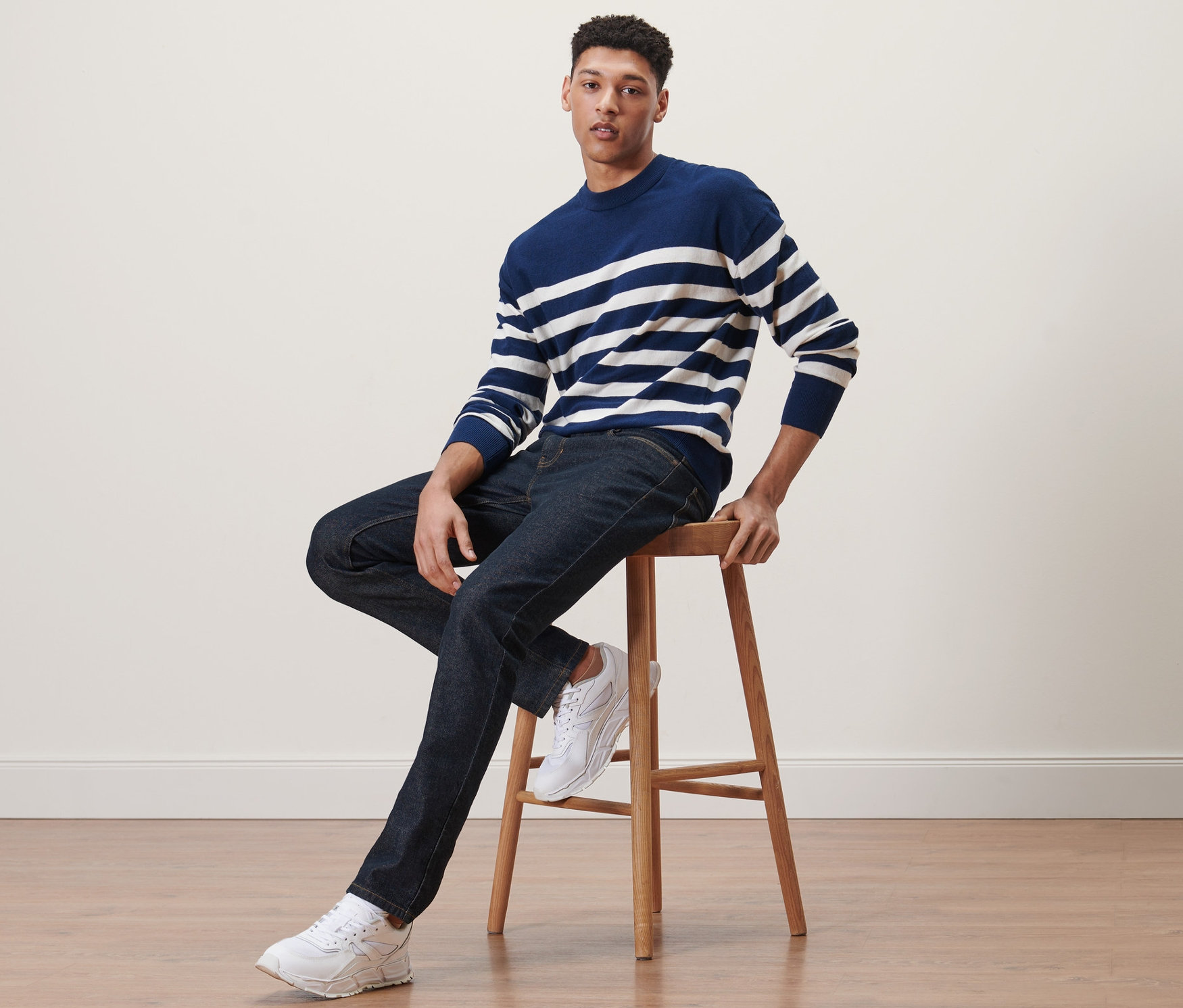 Mann sitzt auf einem Hocker und trägt Jeans.