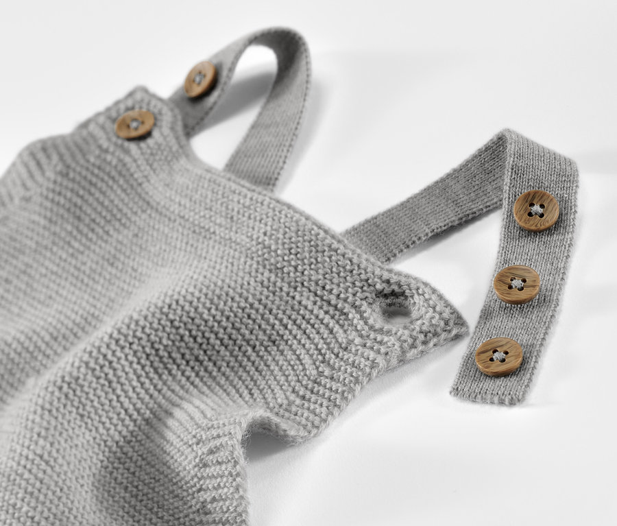 Detailaufnahme einer grauen Baby-Merino-Latzhose mit Holzknöpfen an den Trägern.